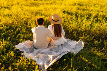 Wall Mural - rear view of unrecognizable young couple in love hugging sitting on beautiful field of green grass i