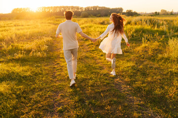 Wall Mural - rear view of unrecognizable happy young couple in love taking each other hand and walking in green m