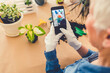 © Jelena Stanojkovic - Beautiful mature woman gardener taking picture of green plants and flowers with smartphone. Home garden workplace home among plants in the home garden, agriculture.