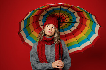 Wall Mural - Young sad woman wear grey sweater scarf hat hold opened colorful umbrella look aside on area isolated on plain red background studio Healthy lifestyle ill sick disease treatment cold season concept.