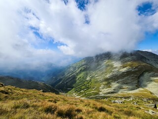 Wall Mural - View of white clouds and blue sky over layered mountain ranges and valley covered with vegetation