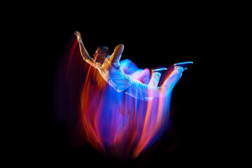 Levitation. One flying, jumping dancer or gymnast performing tricks in the air over black background with mixed neon glowing rays