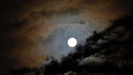 Wall Mural - Full Moon on a cloudy night. Multi-colored clouds fly past the Moon. Dark night sky. Shot with a telephoto lens. Corona (optical phenomenon)