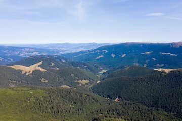 Canvas Print - View of layered mountain ranges covered with dense pine forest and green valley under blue sky