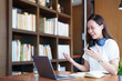 © Jirapong - Portrait of a teenage Asian woman using a computer and notebook to study online via video conferencing on a wooden desk in library