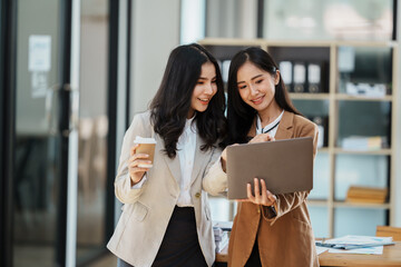 Portrait of beautiful asian businesswoman holding cup of coffee, smiling and looking at camera while sitting at office desk.