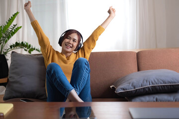 Happy asian woman listening to music from mobile phone while sitting on the rug beside to the sofa at homes, Smiling girl relaxing with headphones in morning, Time to relax.