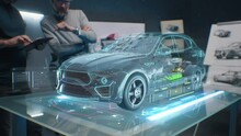 Two Male Engineers Using Digital Tablet App, Developing 3D Model Of A Sustainable Eco Friendly Electric Vehicle. Designers Testing Car Bodys Air Streamline Properties Testing Aerodynamic Parameters