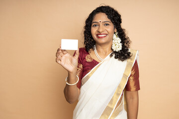 Happy South indian woman wearing white saree holding blank business card or debit credit card isolated on beige background.