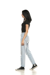 Side view of a young woman in loose jeans walking on white background