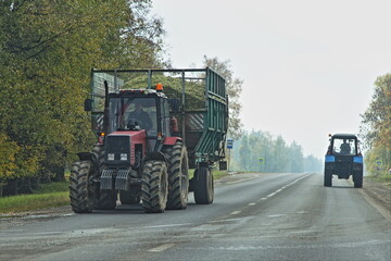 Wall Mural - Big red wheeled tractor transportate a silo in heavy trailer on village asphalted road . Front view . Tractors in work