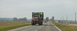 © Ilya - Big red wheeled tractor with heavy trailer on countryside highway road on field