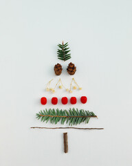 Wall Mural - Christmas tree made with evergreen fir, pine cones, red berries and branches on white background. Minimal holiday flat lay composition. Winter creative concept.