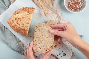 Wall Mural - Woman's hands holding a slice of fresh baked whole grain bread with flax seeds and sesame seeds