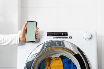 washing machine and hand with blank smartphone indoors