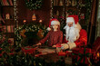 © ZaStock - Santa Clause packs gifts with his little girl assistant while sitting at the table near fireplace.