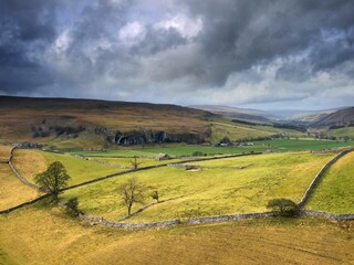 Wall Mural - View of thick clouds over farmhouses and agricultural fields in countryside among hills