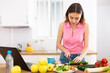 © caftor - Young woman cooking vegetables for dinner and browsing sns on laptop