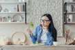 © Liubomir - Portrait of a young beautiful Asian woman sitting in the kitchen at the table, holding a fresh green salad in her fork, sighing, looking at it unhappily. Tired of dieting, hates vegetarianism.