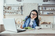 © Liubomir - Dissatisfied and tired of dieting young Asian woman. He is sitting at the table in the kitchen, watching a nutritionist's webinar on a laptop. He holds a fresh salad, looks into the camera.
