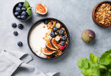 Natural Yogurt With Granola, Berries And Figs In A Black Bowl On A Blue Background With Mint. Healthy And Nutritious Breakfast