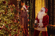 © ZaStock - Little girl with Santa Claus decorating Christmas tree with toys in living room. New Year concept.