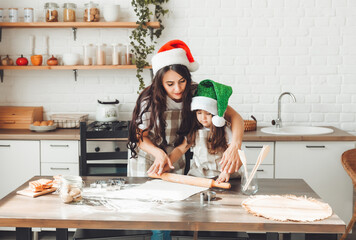 Wall Mural - happy cheerful mother and child in Santa Claus hats are cooking Christmas cookies in the kitchen. new year and Christmas