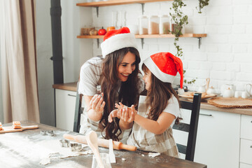 Wall Mural - happy cheerful mother and child in Santa Claus hats are cooking Christmas cookies in the kitchen. new year and Christmas