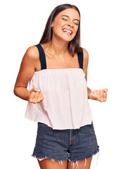 Wall Mural - Young hispanic woman wearing casual clothes very happy and excited doing winner gesture with arms raised, smiling and screaming for success. celebration concept.