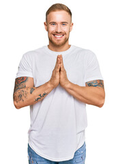 Wall Mural - Young irish man wearing casual clothes praying with hands together asking for forgiveness smiling confident.