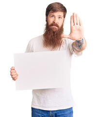 Canvas Print - Handsome young red head man with long beard holding blank empty banner with open hand doing stop sign with serious and confident expression, defense gesture