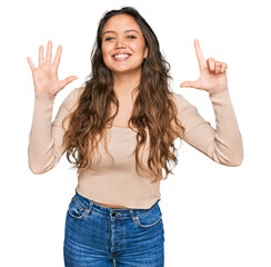 Wall Mural - Young hispanic girl wearing casual clothes showing and pointing up with fingers number seven while smiling confident and happy.