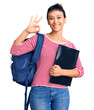 Young woman wearing student backpack holding binder doing ok sign with fingers, smiling friendly gesturing excellent symbol