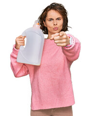 Poster - Young hispanic woman doing laundry holding detergent bottle pointing with finger to the camera and to you, confident gesture looking serious