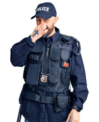 Poster - Young handsome man wearing police uniform smelling something stinky and disgusting, intolerable smell, holding breath with fingers on nose. bad smell