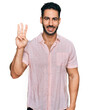 Hispanic man with beard wearing casual shirt showing and pointing up with fingers number three while smiling confident and happy.