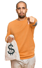 Canvas Print - Hispanic adult man holding dollars bag pointing with finger to the camera and to you, confident gesture looking serious