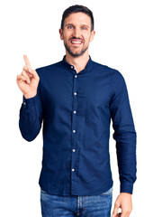 Canvas Print - Young handsome man wearing casual shirt with a big smile on face, pointing with hand finger to the side looking at the camera.