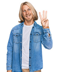 Wall Mural - Caucasian man with blond long hair wearing casual denim jacket showing and pointing up with fingers number three while smiling confident and happy.