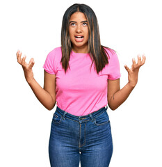 Poster - Young latin girl wearing casual clothes crazy and mad shouting and yelling with aggressive expression and arms raised. frustration concept.