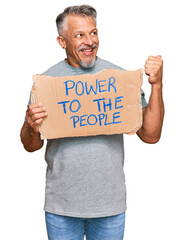 Canvas Print - Middle age grey-haired man holding power to the people banner pointing thumb up to the side smiling happy with open mouth