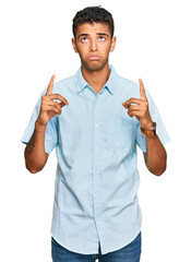 Poster - Young handsome african american man wearing casual clothes pointing up looking sad and upset, indicating direction with fingers, unhappy and depressed.