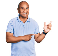 Hispanic middle age man wearing casual t shirt smiling and looking at the camera pointing with two hands and fingers to the side.