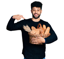 Sticker - Young arab man with beard holding wicker basket with bread smiling happy pointing with hand and finger