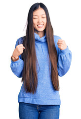 Wall Mural - Young beautiful chinese woman wearing casual turtleneck sweater excited for success with arms raised and eyes closed celebrating victory smiling. winner concept.