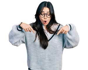 beautiful hispanic woman wearing casual sweater and glasses pointing down with fingers showing adver
