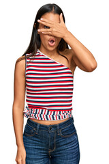 Sticker - Beautiful hispanic woman wearing casual clothes peeking in shock covering face and eyes with hand, looking through fingers with embarrassed expression.