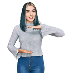 Wall Mural - Young modern girl wearing casual sweater gesturing with hands showing big and large size sign, measure symbol. smiling looking at the camera. measuring concept.