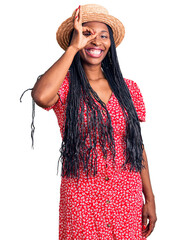 Sticker - Young african american woman wearing summer hat doing ok gesture with hand smiling, eye looking through fingers with happy face.