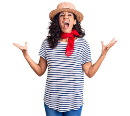 Wall Mural - Middle age beautiful woman wearing casual striped t shirt and summer hat crazy and mad shouting and yelling with aggressive expression and arms raised. frustration concept.